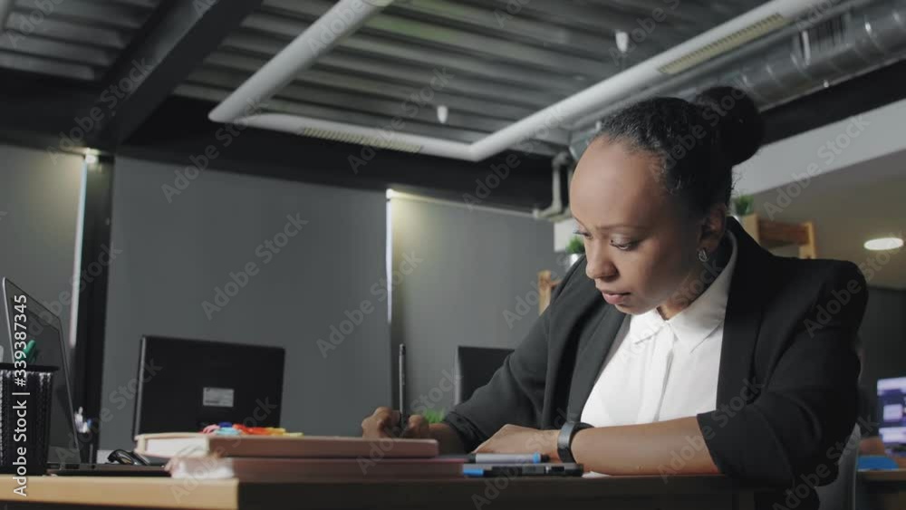 Side view of young african american woman typing on laptop in office then writing in notebook Side view of young african american woman typing on laptop in office then writing in notebook