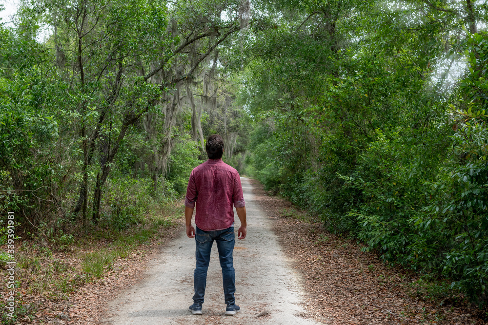 young man with brown hair and beard wearing red button down breathes in a breath of fresh air immersing himself in a nature path to social distance himself in order to stay healthy and alive. young man with brown hair and beard wearing red button down breathes in a breath of fresh air immersing himself in a nature path to social distance himself in order to stay healthy and alive.