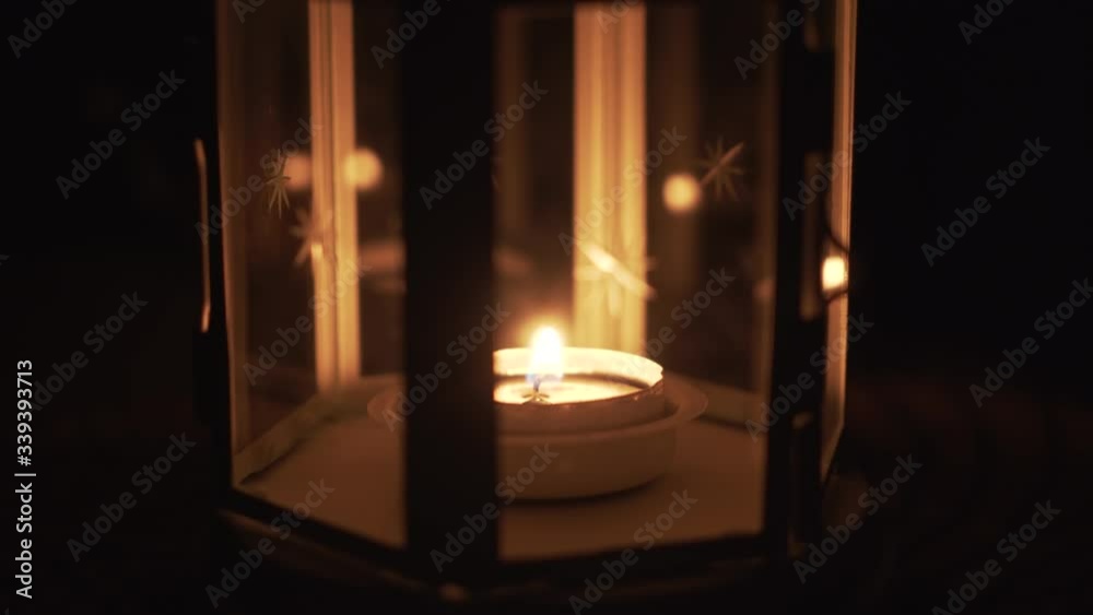 Lantern with candle close up. White lantern with stars and burning candle inside on table outside at night. Lantern with candle close up. White lantern with stars and burning candle inside on table outside at night.