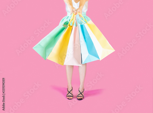 The back of woman low body part wore blue skirt and black high heels. Carrying a shopping bag in many pastel colors on pink background selective focus