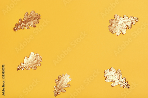 Creative layout made of golden oak leaves on yellow paper background. Minimal autumn concept with copy space.