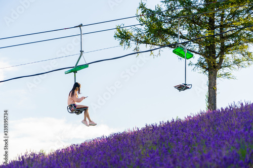 Asian girl sits on ski lift chairs moving to the mountain in Choei lavender farm at sunset time in Furano, Hokkaido, Japan. photo