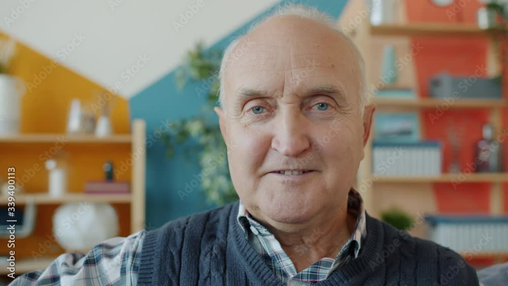 Close-up portrait of good-looking retired gray-haired man looking at camera at home with light smile. Positive emotions and retirement concept. Close-up portrait of good-looking retired gray-haired man looking at camera at home with light smile. Positive emotions and retirement concept.