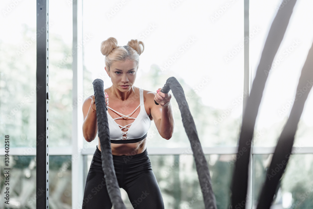 Obraz premium Strong attractive woman exercising with battle rope in gym