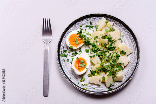 Boiled potatoes with herbs and soft-boiled eggs in a plate on grey concrete background. Selective focus