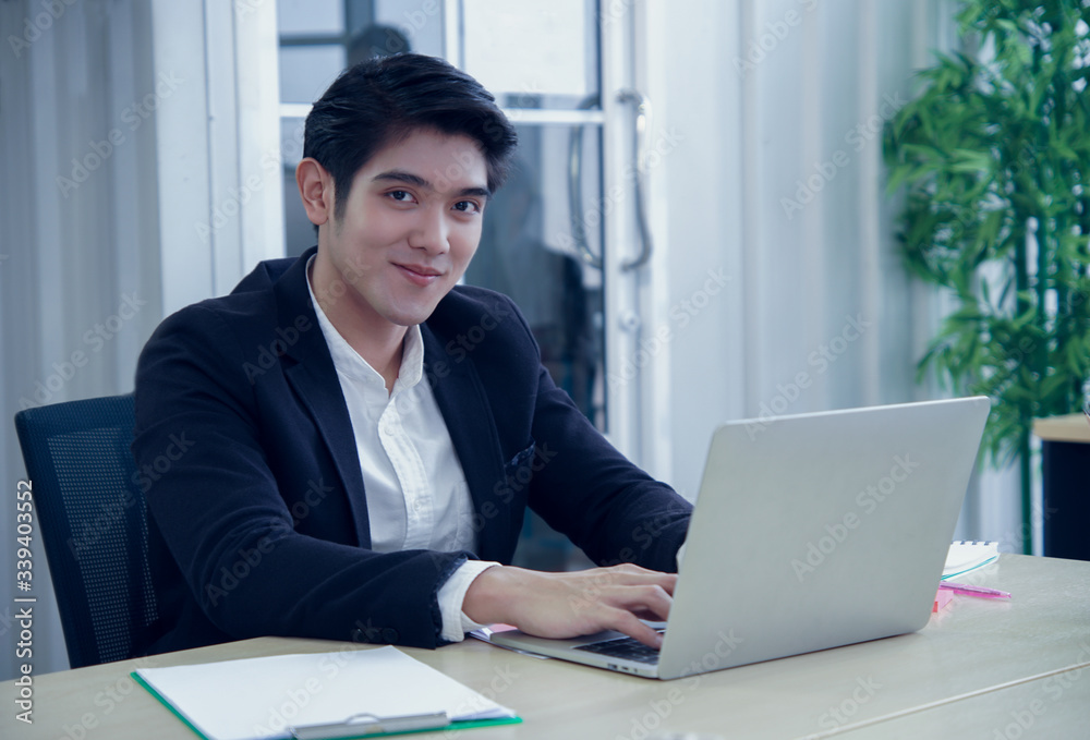 Portrait of asian smart young handsome businessman smiling at the camera and sitting at his desk in the office Portrait of asian smart young handsome businessman smiling at the camera and sitting at his desk in the office