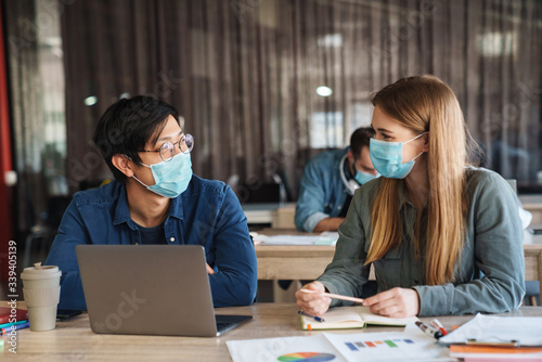 Image of students in protective mask talking while studying with laptop