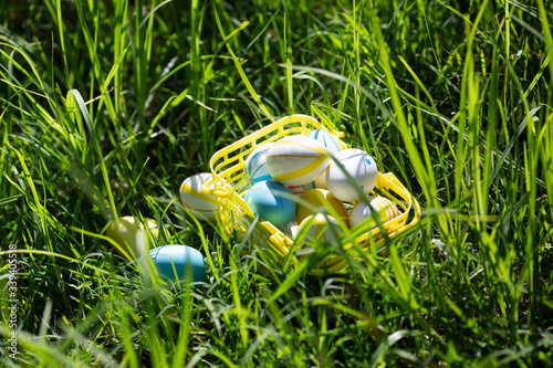 Easter eggs lay in a yellow basket on the green grass on a sunny day. Happy easter day.