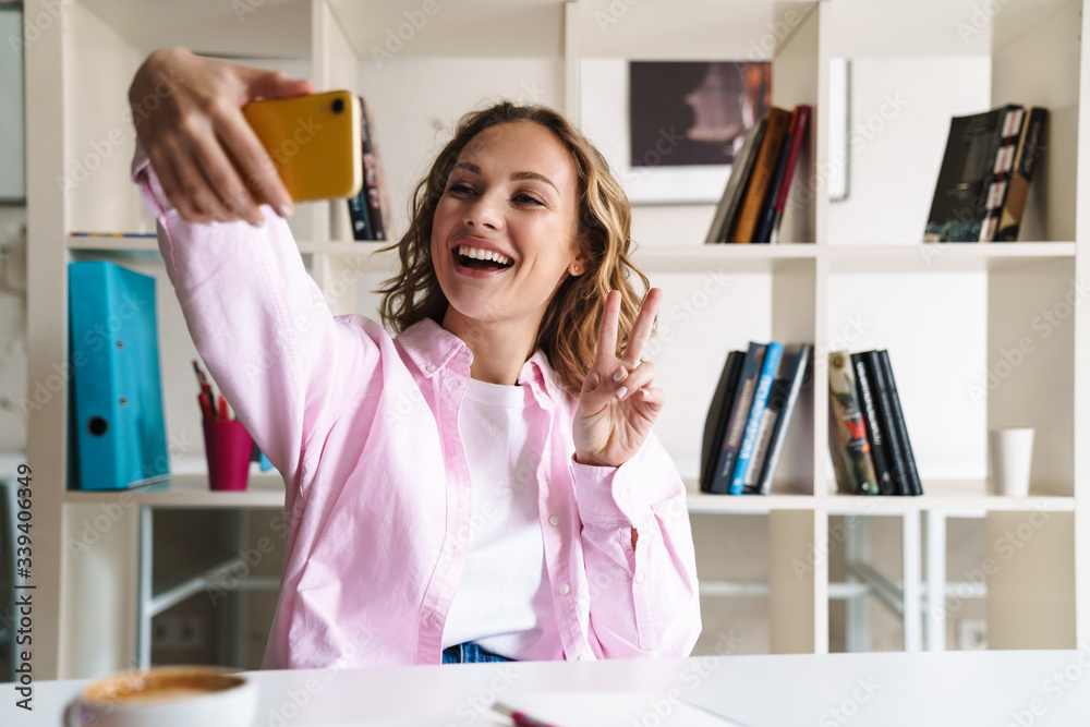 Photo of woman taking selfie on cellphone and gesturing peace sign Photo of woman taking selfie on cellphone and gesturing peace sign