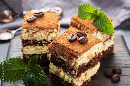 Pieces of tiramisu cake with delicate cream, coffee beans and mint leaves.