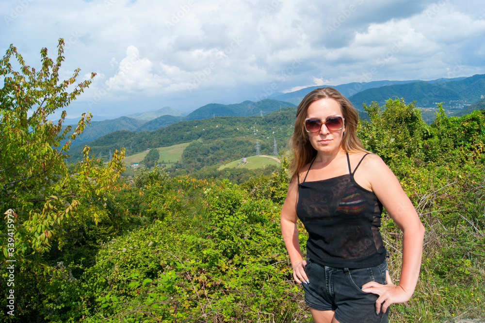 Portrait of an adult woman of forty years against the backdrop of the Caucasian mountains and blue sky in white clouds.