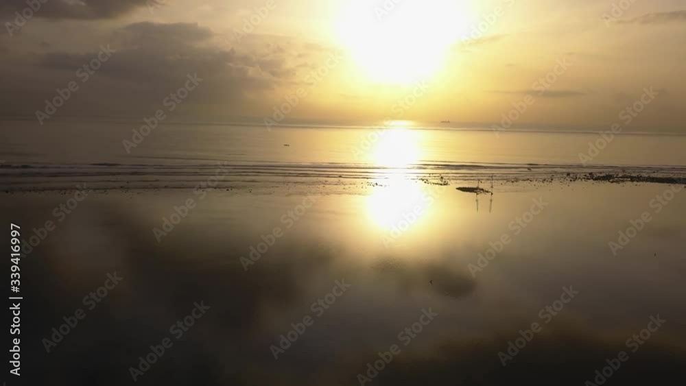 Drone video of a calm beach, at sunrise with the sun reflecting in the water, flying backwards Drone video of a calm beach, at sunrise with the sun reflecting in the water, flying backwards