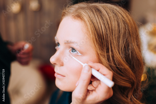 Makeup artist makes white fantasy makeup for a young woman with brown hair