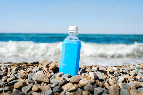 empty plastic blue bottle on a rocky beach against the background of a raging blue sea with waves and foam.