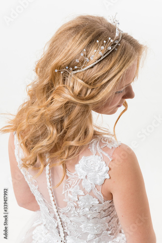 Romantic young bride isolated on white in white lace wedding dress with makeup and wavy blonde hair with pearl jewelry getting ready in bride's morning. Fine art wedding. 