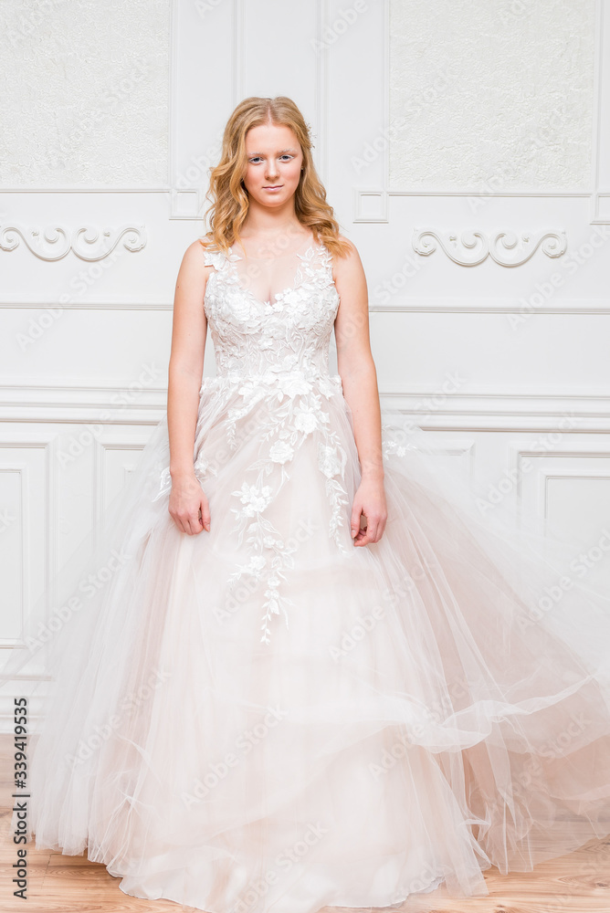 Romantic young bride in elegant hotel room in white lace wedding dress with makeup and wavy blonde hair getting ready in bride's morning. Fine art wedding. Romantic young bride in elegant hotel room in white lace wedding dress with makeup and wavy blonde hair getting ready in bride's morning. Fine art wedding.