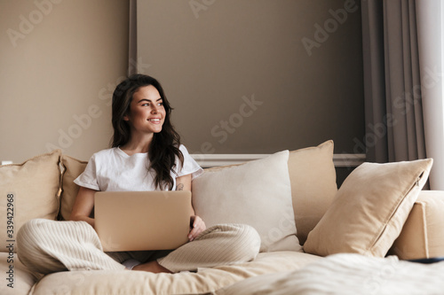 Billede på lærred Beautiful young brunette woman relaxing on a couch at home