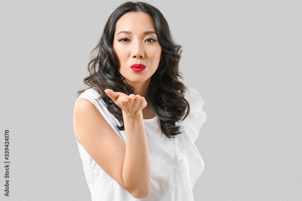Young Asian woman with beautiful hair blowing kiss on grey background Young Asian woman with beautiful hair blowing kiss on grey background