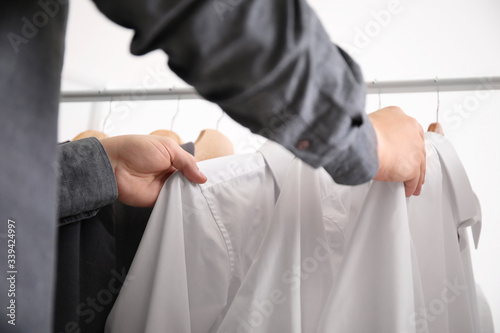 Young male stylist choosing clothes from rack, closeup