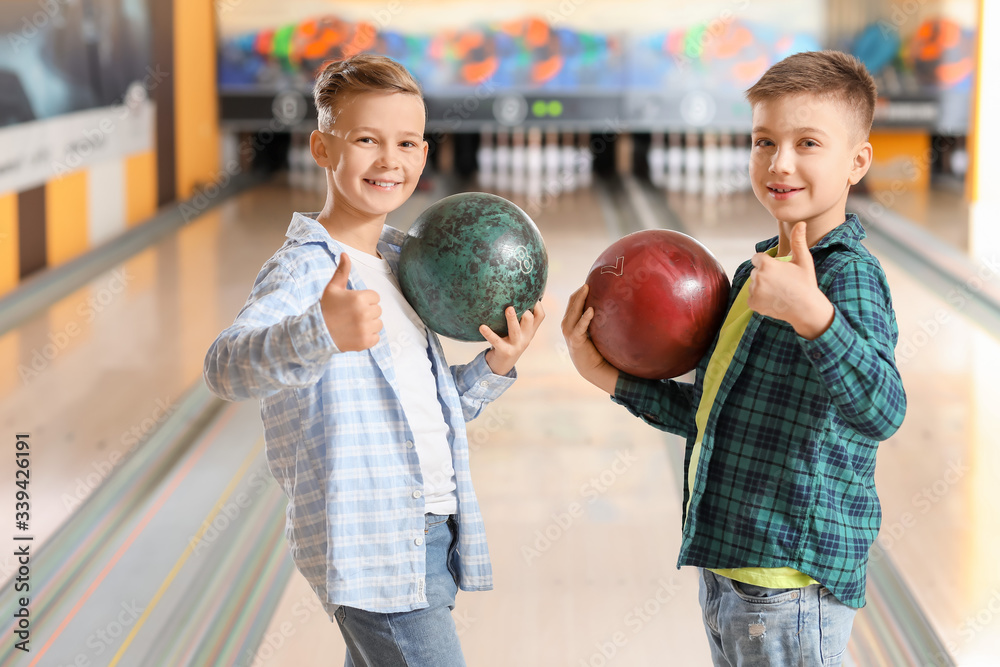 Fototapeta premium Two happy young boys holding bowling balls and giving thumbs up at a modern bowling alley, the children are smiling, enjoying a leisure activity together
