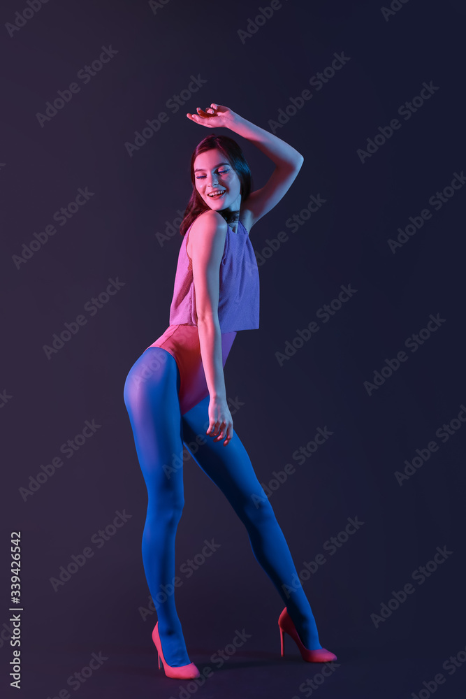 Beautiful young woman dancing against dark background