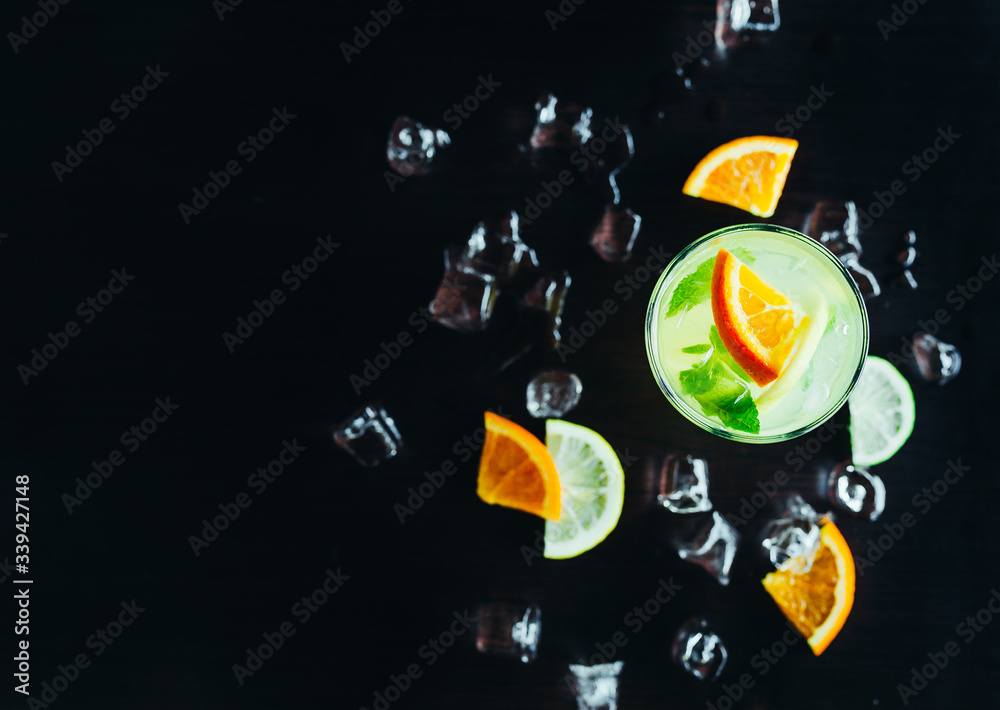 top of view of glass with cocktail and ice with lime and orange slice on black background