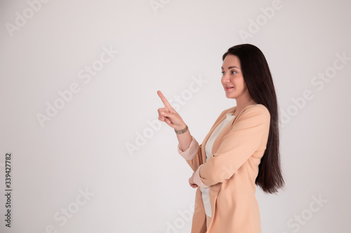 Successful business woman on grey background with copy space. girl in beige strict points with your finger hand on the left
