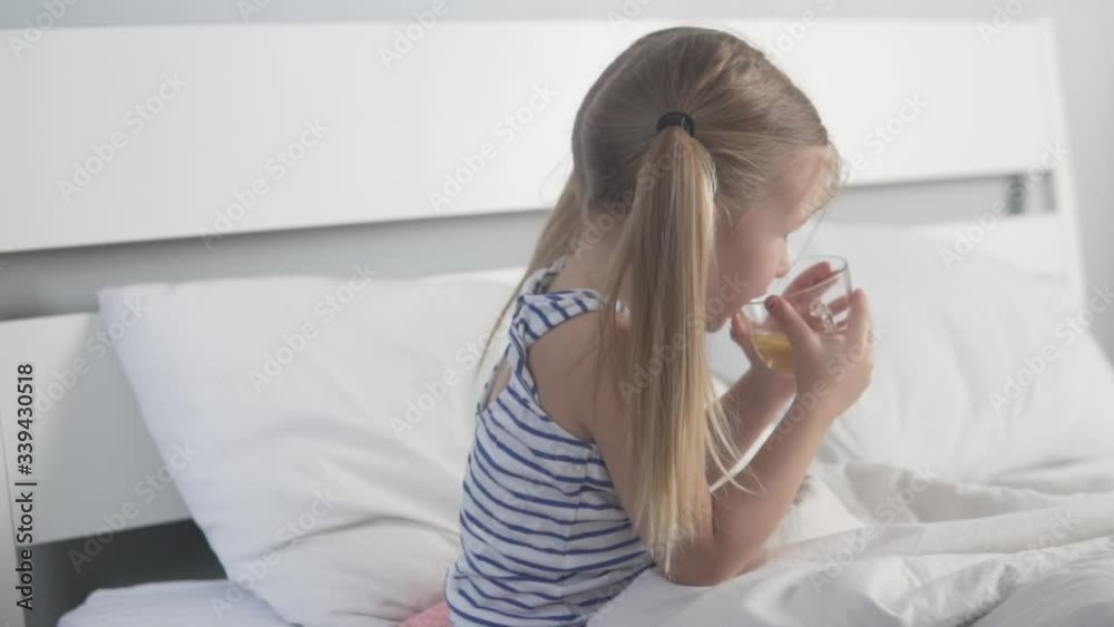 A little girl drinks tea with lemon in a bed. The child has been cured of the virus A little girl drinks tea with lemon in a bed. The child has been cured of the virus