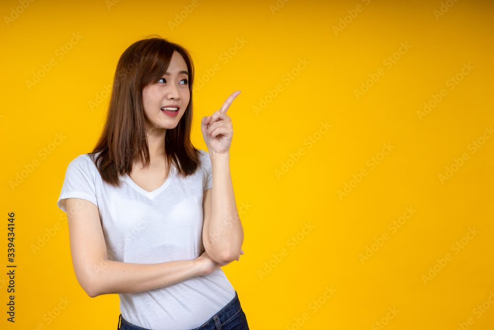 Young elegant Asian woman smiling and pointing to empty copy space isolated on yellow background Young elegant Asian woman smiling and pointing to empty copy space isolated on yellow background