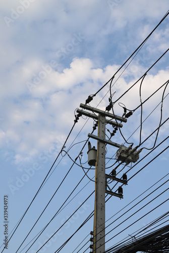 Closeup of electricity wire, cable, poles and high voltage transformer beside the street with cloudy blue sky background. Vertical view. © Amphon