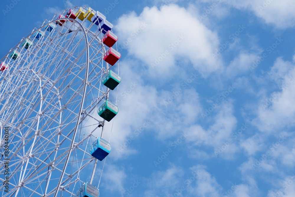 Ferris wheel in amusement park against blue sky and white clouds Ferris wheel in amusement park against blue sky and white clouds