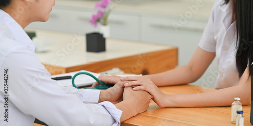 Slika na platnu Cropped image of Medical students comforting together while sitting at wooden working desk over comfortable learning space as background