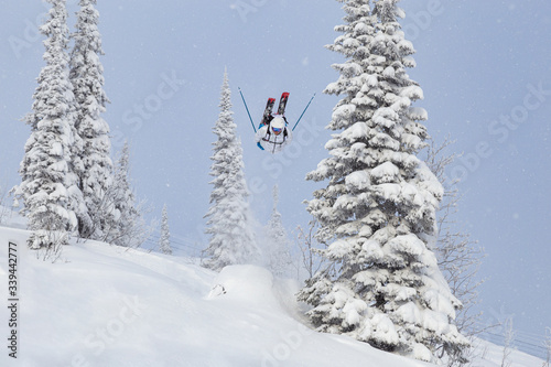 a Freerider in bright gear jumps between Christmas trees with a backflip element. prof skier in a beautiful flight at high altitude. Winter fun at the ski resort. Good powder day. Funny skiing