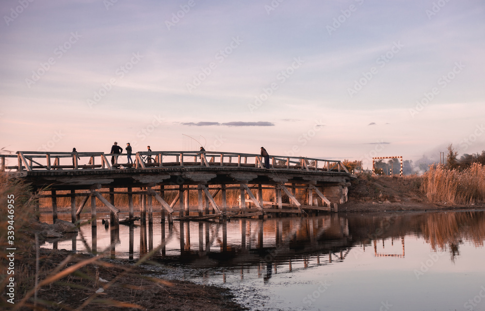 People fishing on an old wooden bridge at sunset