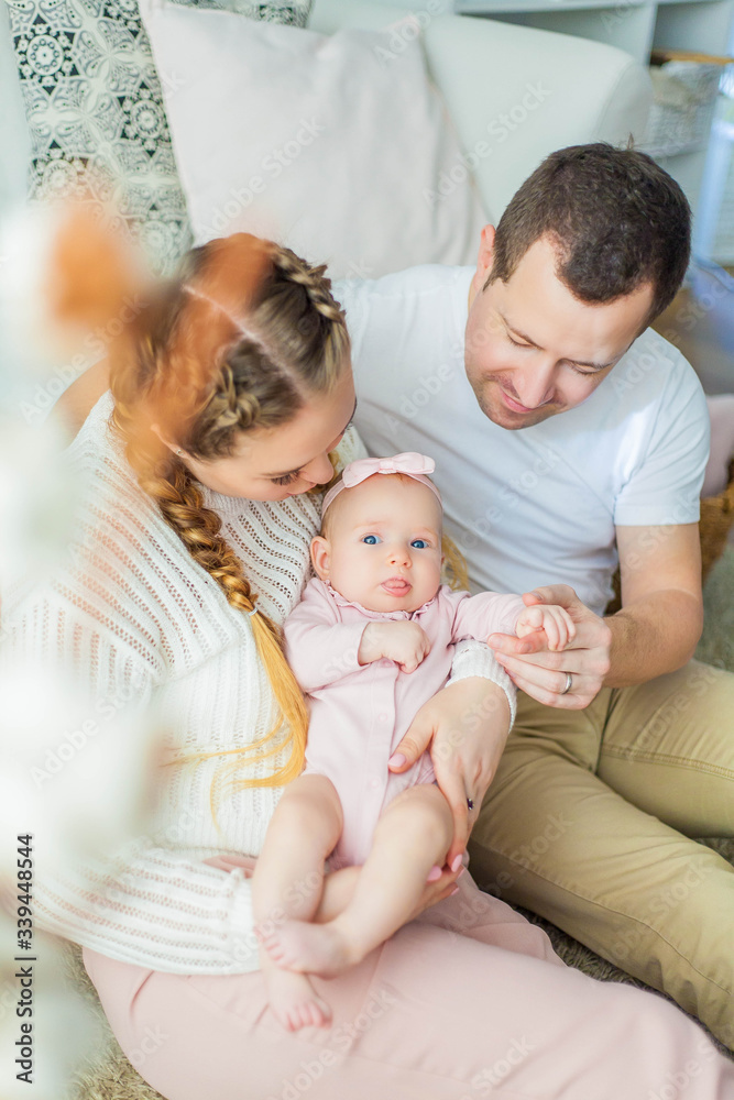 Beautiful young parents are holding their little newborn daughter in their arms. Blue-eyed little girl of 2 months. Baby