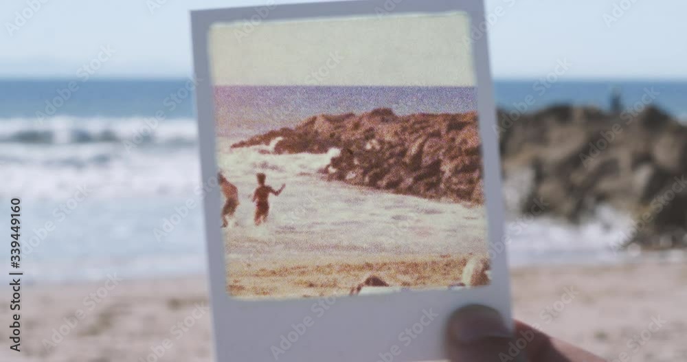 Polaroid frame held up to camera revealing vintage footage of people playing and frolicking at beach
