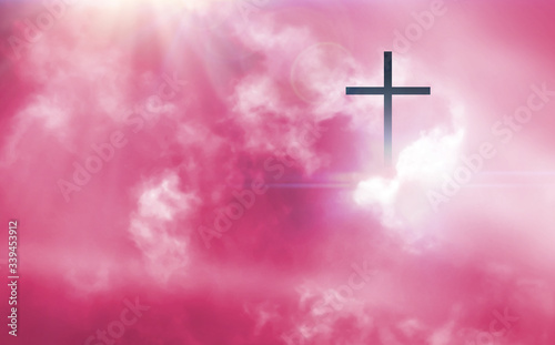 The Christian cross looks bright in the pink sky, with soft white clouds and beautiful light which leads to peace and heaven.