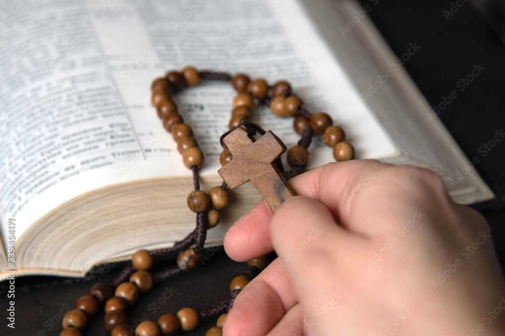 Fototapeta premium Woman holding and praying on rosary, on Bible background