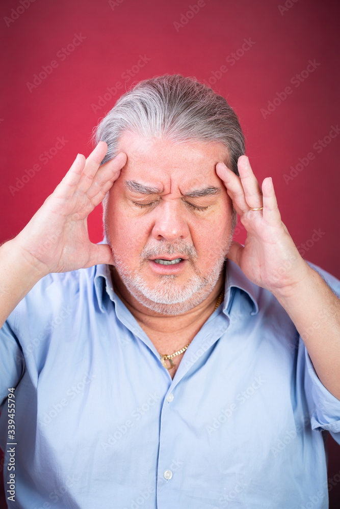 Man headshot portrait. He is in despair with both hands on his head and with eyes closed. The background is lighted with red color. Man headshot portrait. He is in despair with both hands on his head and with eyes closed. The background is lighted with red color.