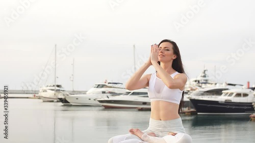 Attractive woman in lotus pose sitting at marine piers with seaboats and yachts. Concept of calmness and meditation. photo