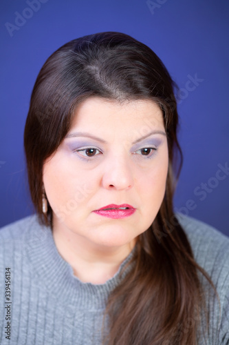 Woman studio closeup portrait. She looks preoccupied and down. The background is lighted with blue color.