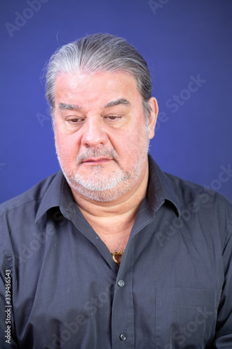 Man studio closeup portrait. He is serious and looking to the camera. His face shows some disappointment around him. The background is lighted with blue color.
