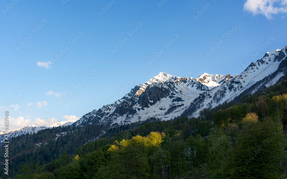 Fototapeta premium Beautiful snow-capped mountains against the blue sky in Sochi, Krasnodar territory, Krasnaya Polyana resort village, the Caucasus mountain range