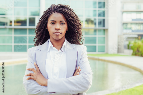 Confident young businesswoman looking at camera. Portrait of serious African American businesswoman standing with crossed arms on street. Business concept
