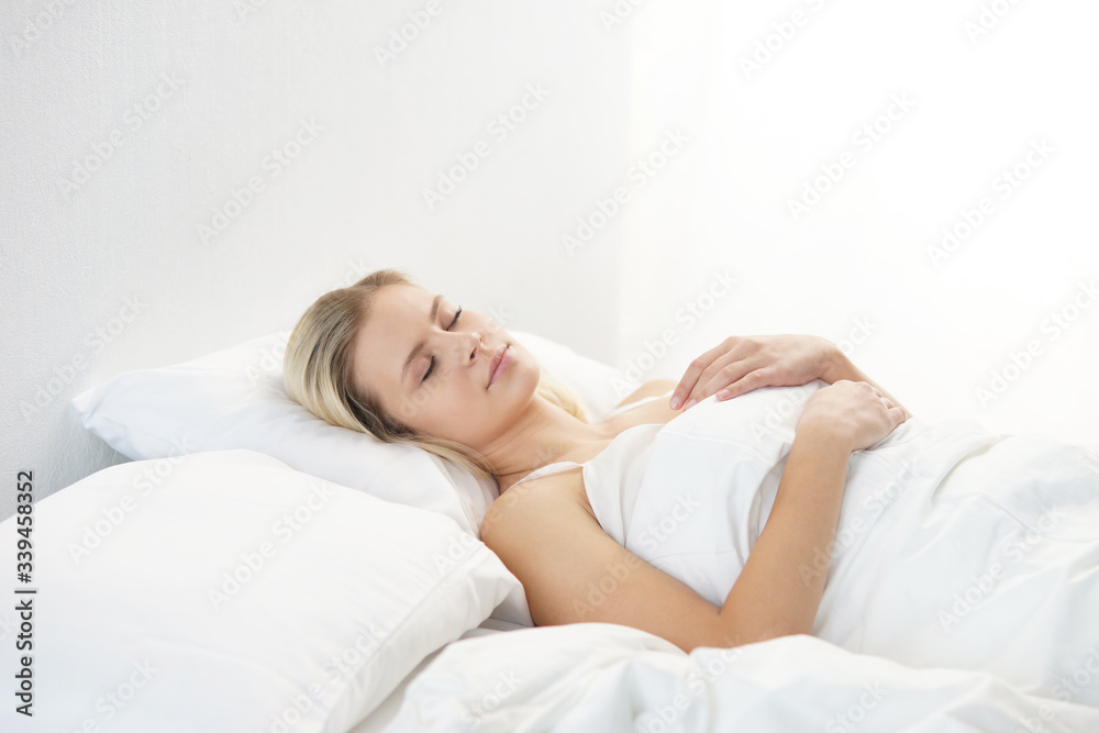 Young woman lying in the bed. Beautiful blond sleeping girl. Morning in the bedroom, daylight from the window. Health and rest. Young woman lying in the bed. Beautiful blond sleeping girl. Morning in the bedroom, daylight from the window. Health and rest.