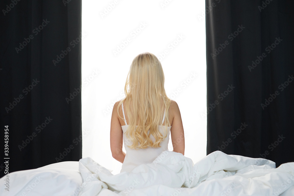 Young woman in the bed. Beautiful blond girl wakes up. Morning in the bedroom, daylight from the window. Health and rest.