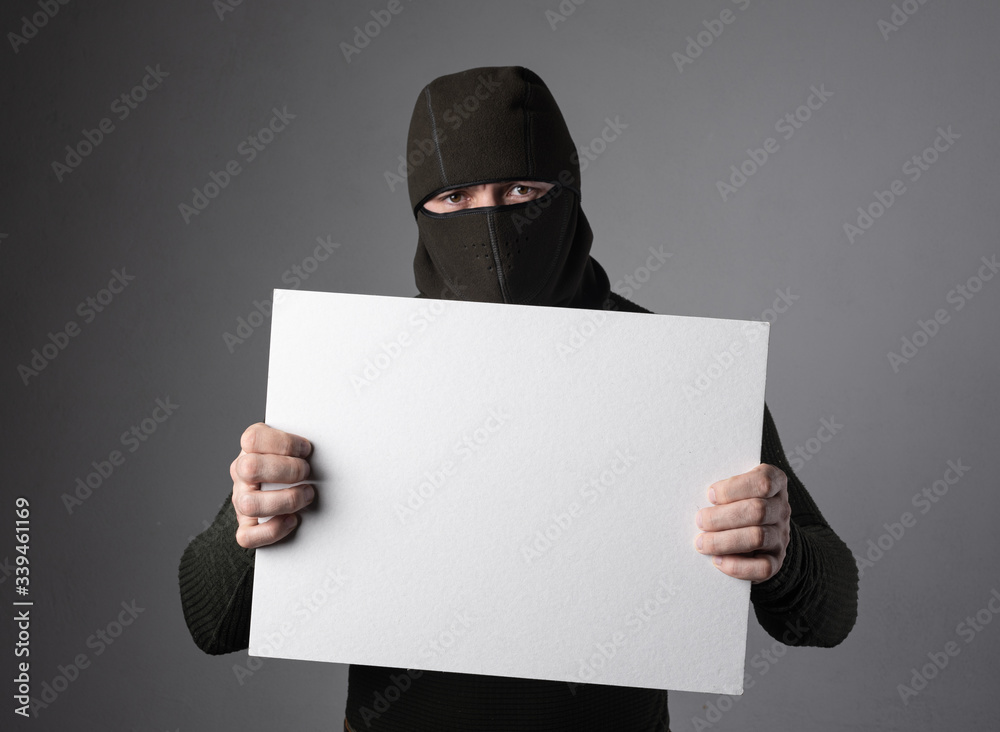 An extremist in a balaclava holds a white tablet in his hands, with a place for writing text An extremist in a balaclava holds a white tablet in his hands, with a place for writing text