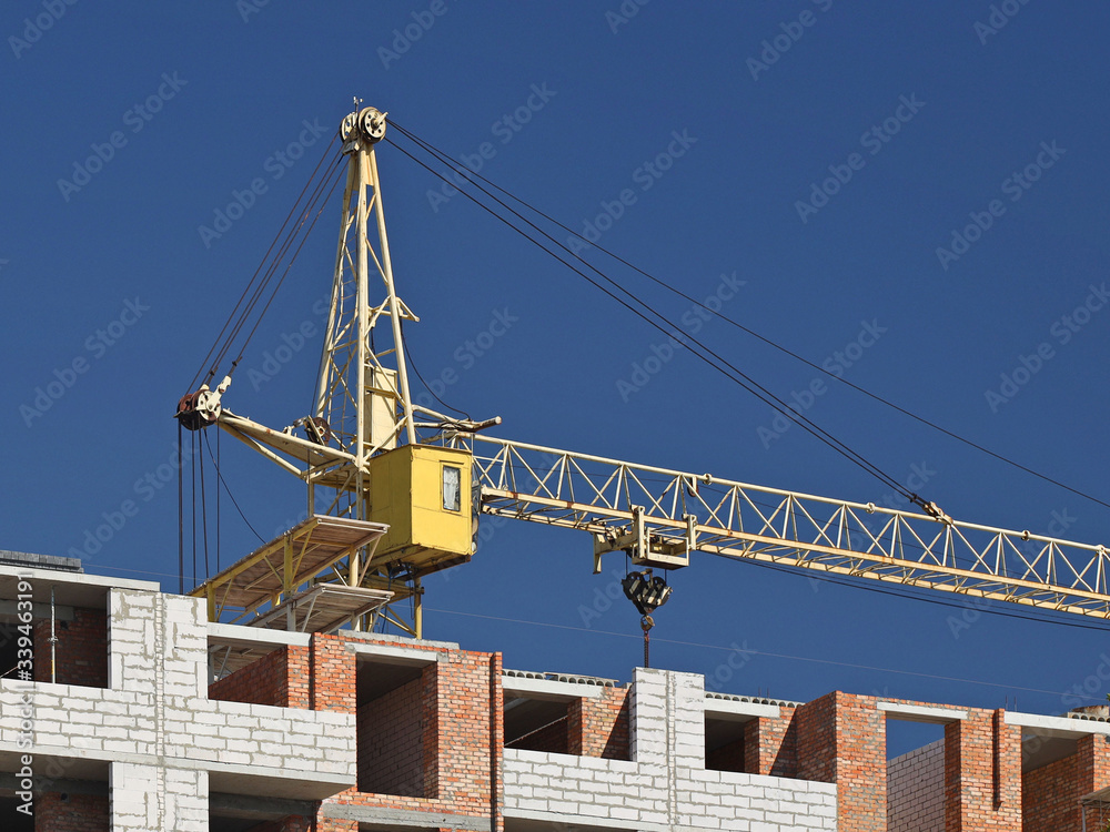 Two crane operators in overalls repair a high-rise tower crane working during the construction of a multi-storey building. Risky work at height. Lifting heavy building materials. City development