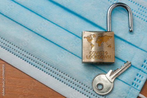 Coronavirus world lockdown end: an open lock with a world map and the word lockdown engraved and a key on a light blue surgical mask. photo