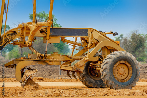 Close up of Motor grader clearing and leveling construction site surface. Grader industrial machine on road construction work.